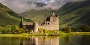 Die Ruinen von Kilchurn Castle spiegeln sich im ruhigen Wasser des Loch Awe, umgeben von nebligen grünen Hügeln in Argyll, Schottland.