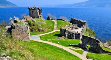 Ruins of a medieval castle perched on a clifftop overlooking the deep blue waters of Loch Ness in the Scottish Highlands.