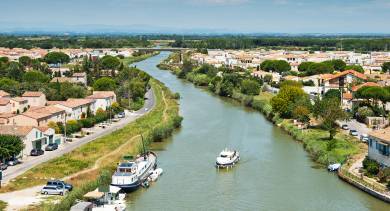 View of a canal winding through a southern French village in Camargue, with boats cruising between terracotta-roofed houses.