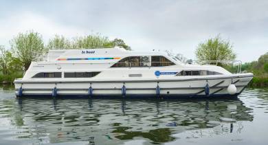 Side view of the Classique Star on a peaceful canal, reflecting cleanly in the water with lush greenery in the background.