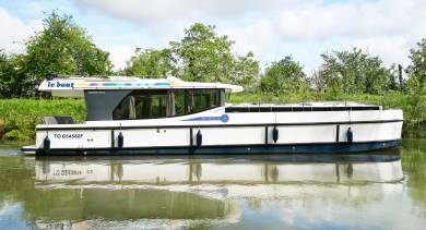 Side view of the Horizon 5 gliding on a peaceful canal with clean lines, panoramic windows, and reflections mirrored perfectly on the water.
