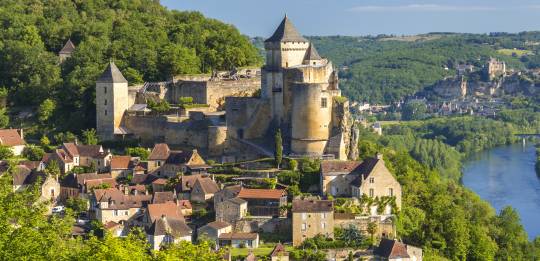 A medieval castle perched above a river and hilltop town in Aquitaine.