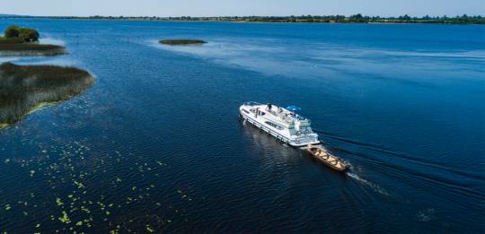 White cruiser boat towing a wooden canoe on Lough Key under clear blue skies.
