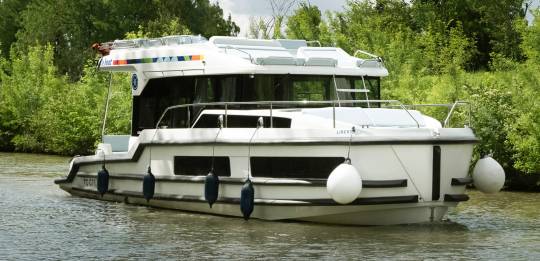 Liberty boat gliding gently on the water, with lush foliage along the banks and soft summer skies above.
