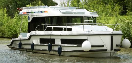 Liberty boat gliding gently on the water, with lush foliage along the banks and soft summer skies above.