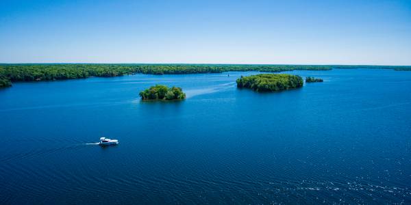 Una barca Horizon naviga vicino a piccole isole boschive sul Canale Rideau, l’acqua di un blu profondo si estende verso l’orizzonte.