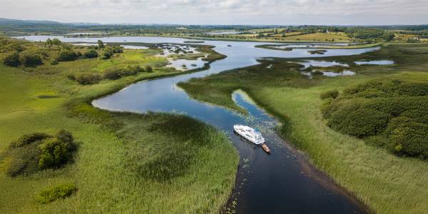 Aerial view of a white cruiser boat sailing through winding marshes on the River Shannon.