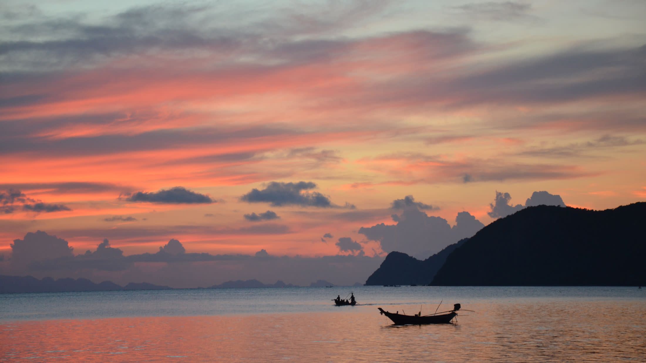 a sunset over a body of water with a mountain in the background
