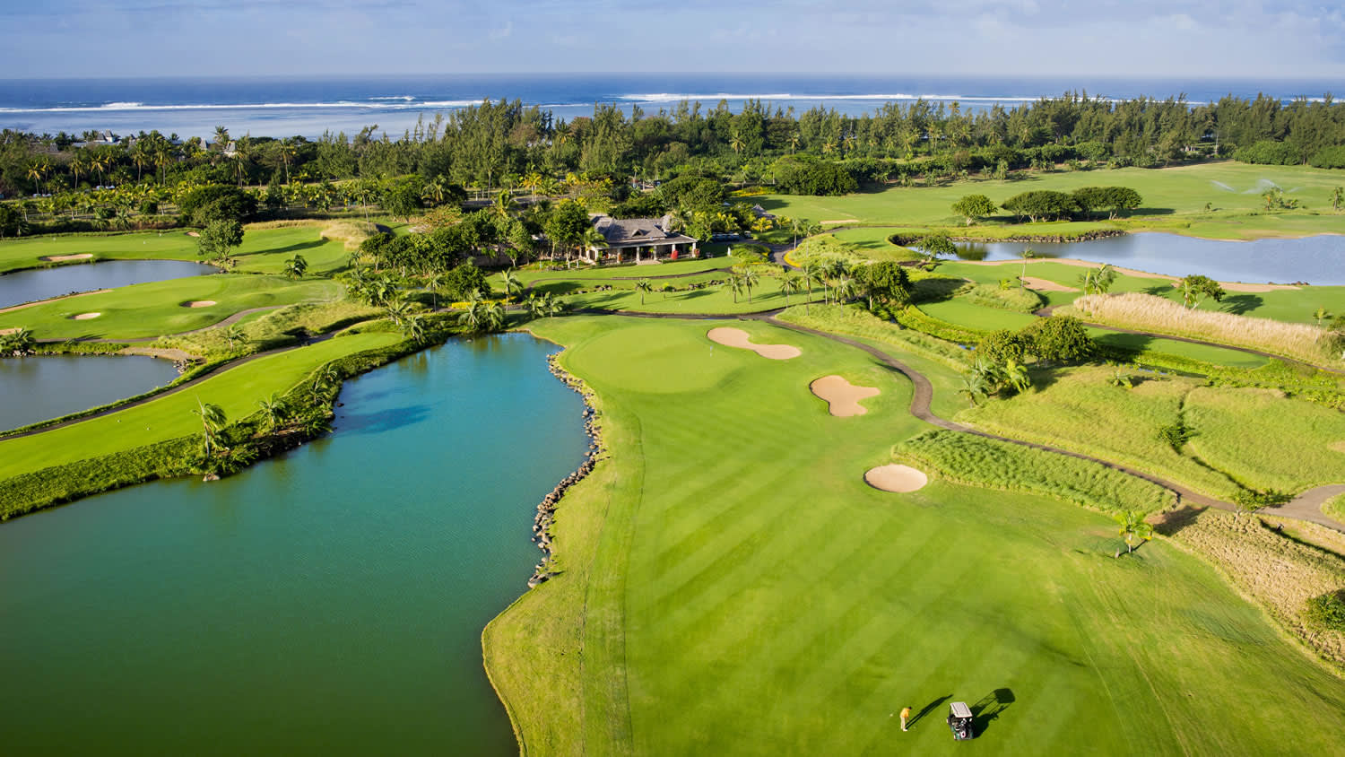 a lush green field next to a body of water with The Golf Club at Harbor Shores in the background