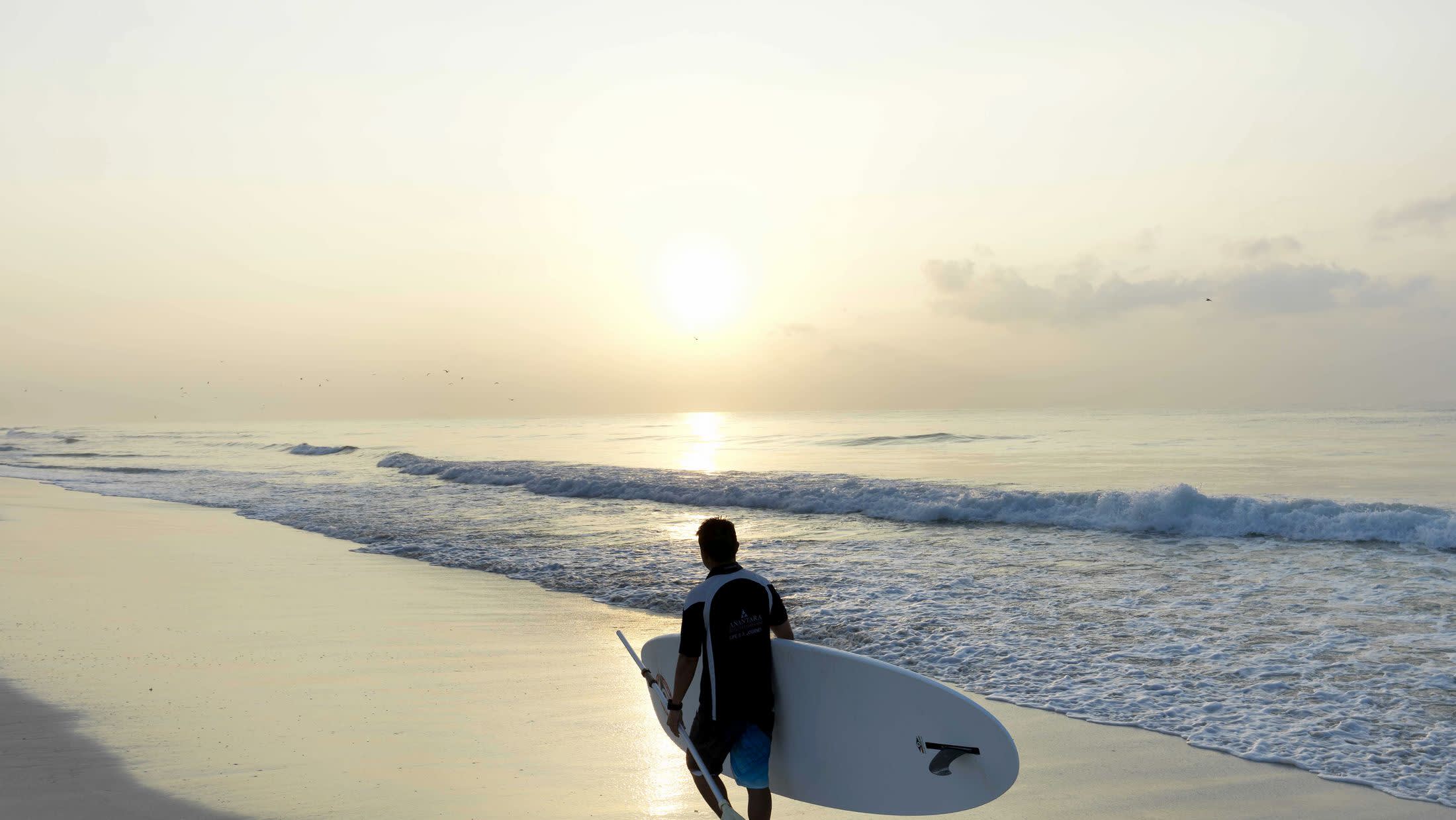 a man in a wet suit standing on a beach holding a surf board