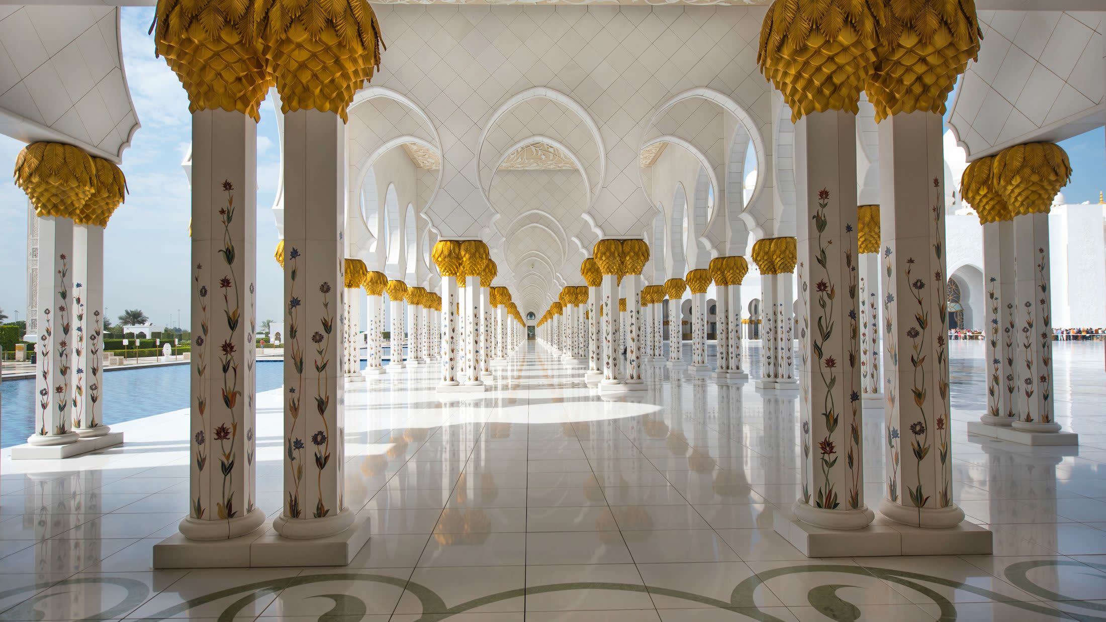 a clock hanging from the ceiling with Sheikh Zayed Mosque in the background