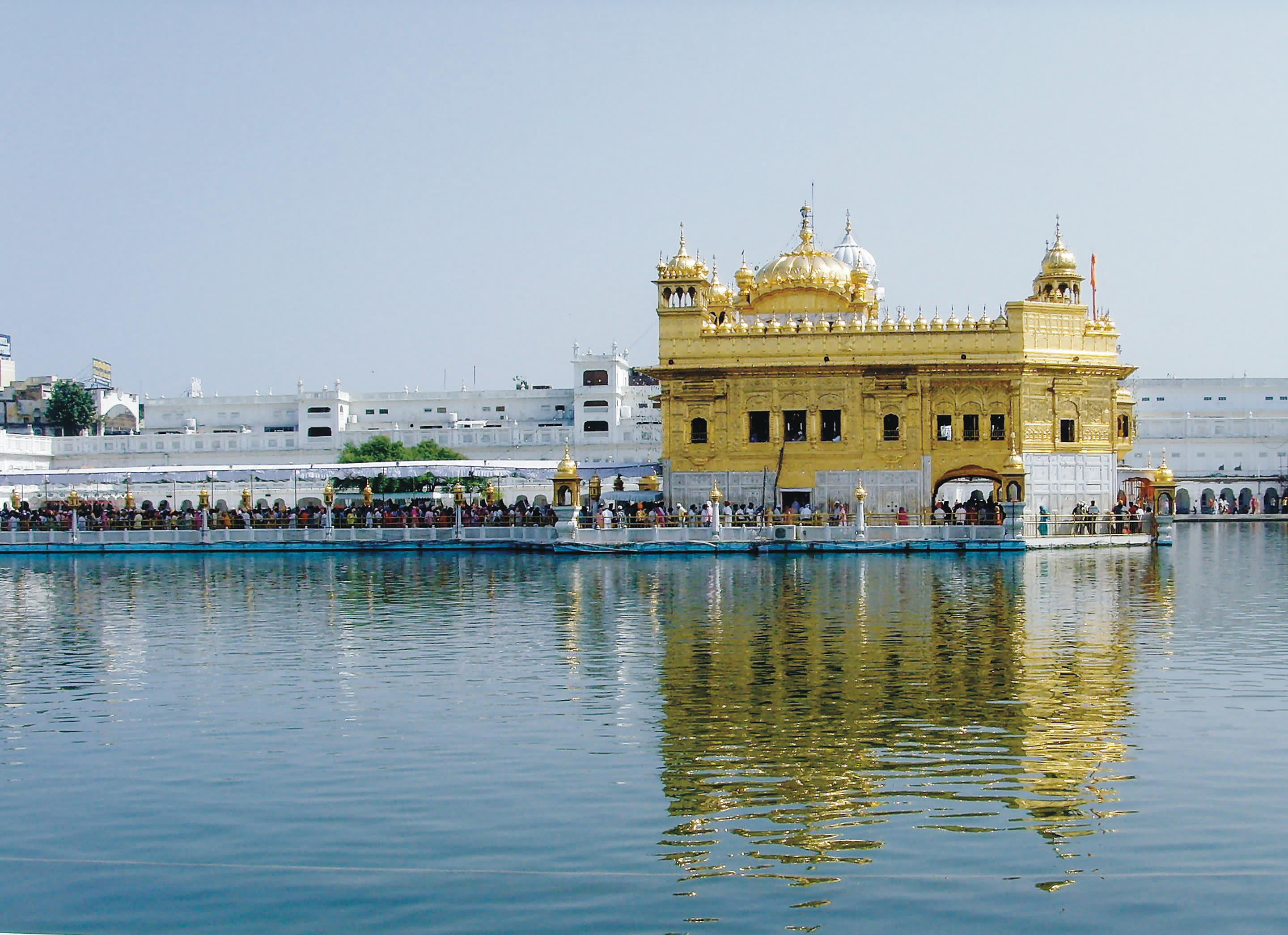 a large yellow boat in the water with Harmandir Sahib in the background