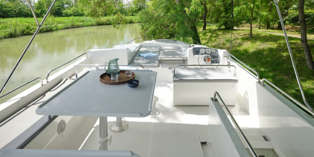 Spacious upper deck on the Horizon 5 with helm seating, shaded dining table, and views of a tranquil tree-lined canal.