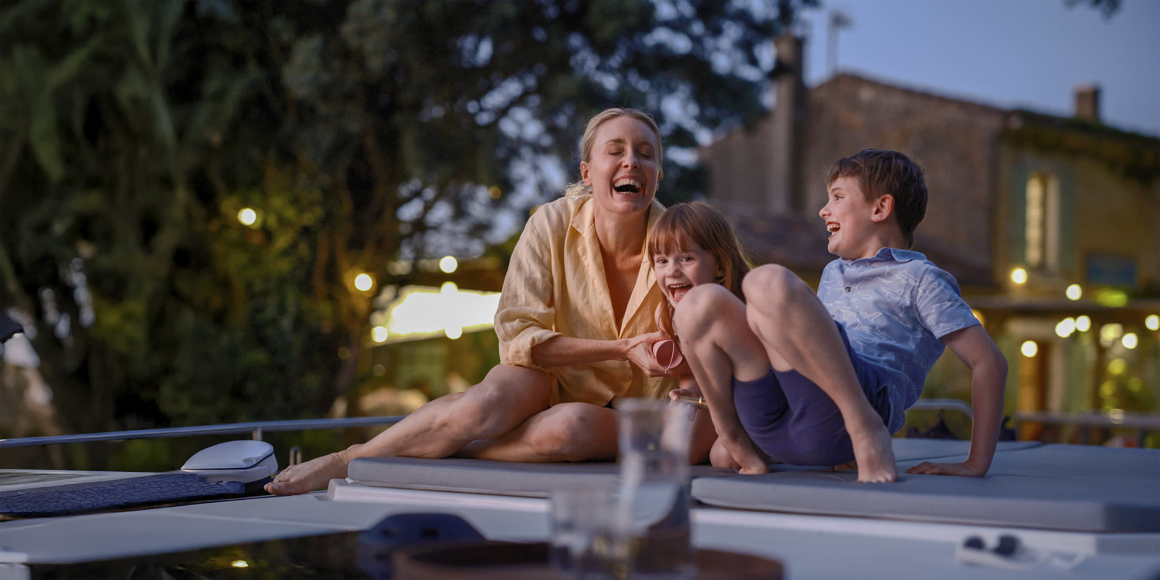 Mutter und Kinder lachen gemeinsam auf dem Boot während eines entspannten Zwischenstopps am Abend.