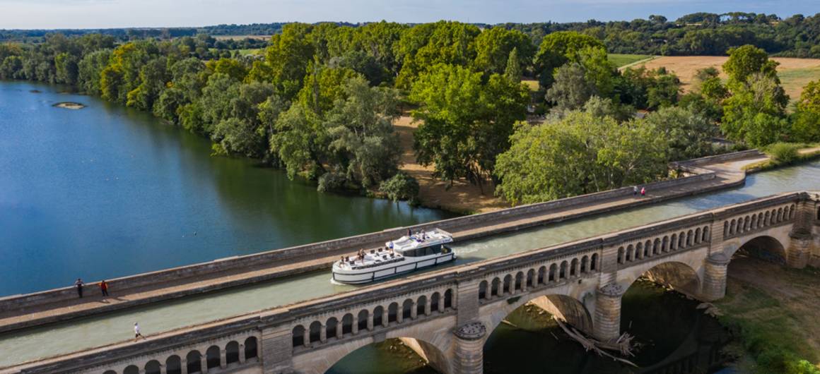 A canal boat cruises across the Orb Aqueduct on the Canal du Midi, surrounded by peaceful countryside.