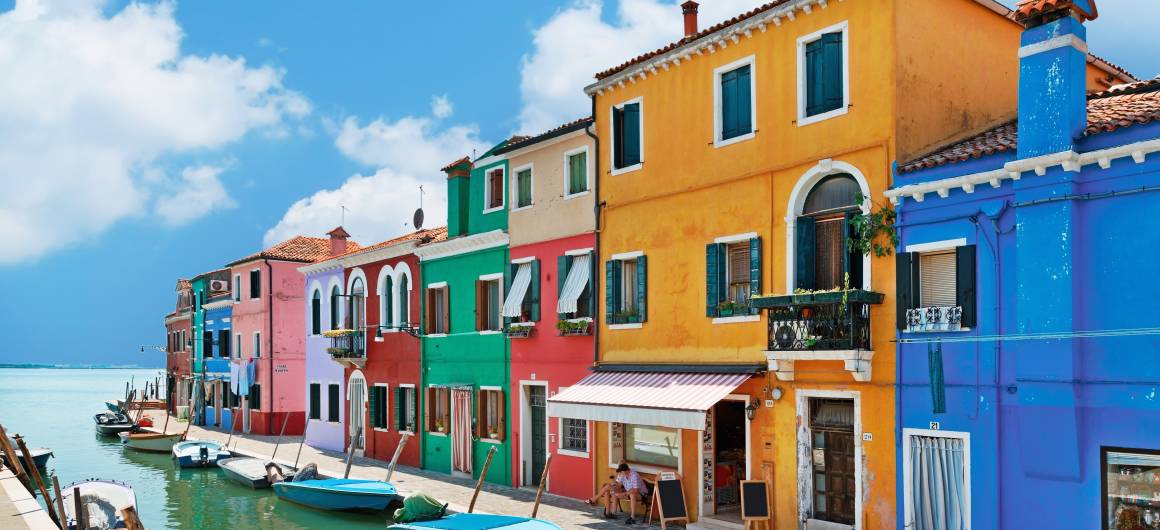 Row of brightly coloured houses reflected in a quiet canal on the island of Burano in the Veneto region.