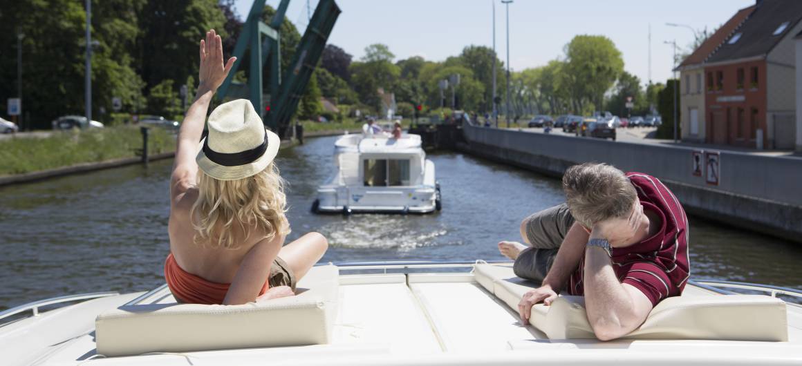 Couple relaxing on the Vision boat’s deck while cruising past a raised bridge on a sunny day.