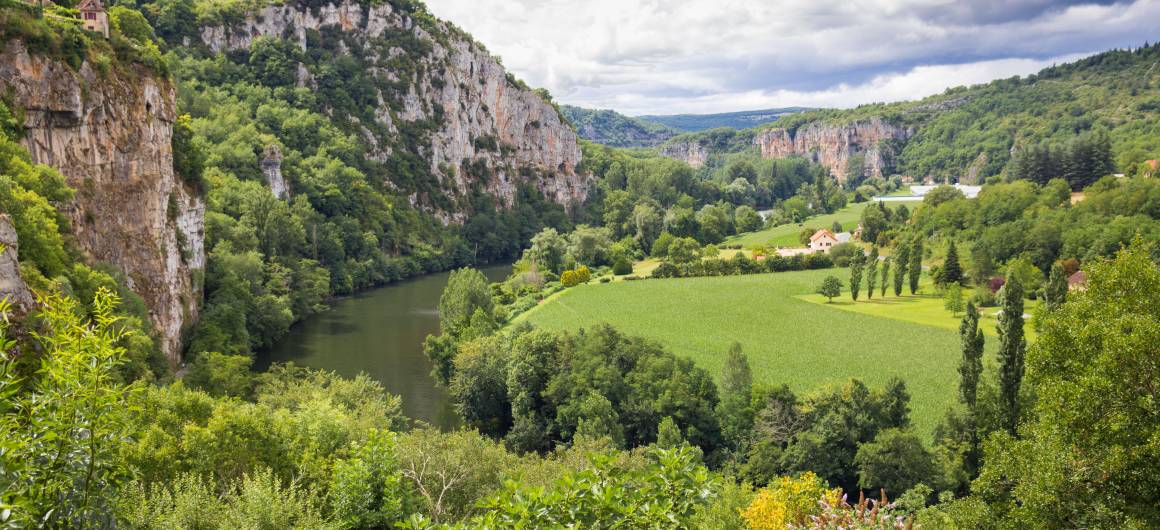 Panoramic view of a green valley with cliffs and the Lot River winding through fields and forests.