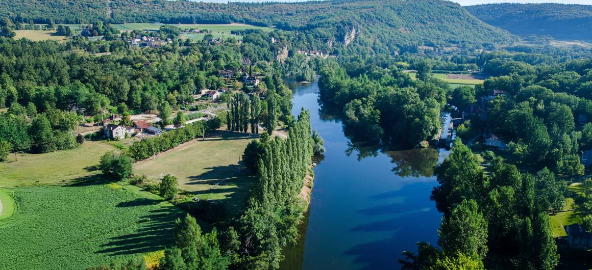Aerial view of the Lot River winding through lush countryside and forested hills under a clear blue sky.