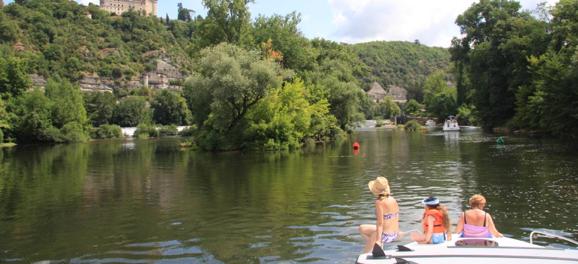 Three people seated at the bow of a boat, enjoying a peaceful cruise through a wooded stretch of the Lot River.