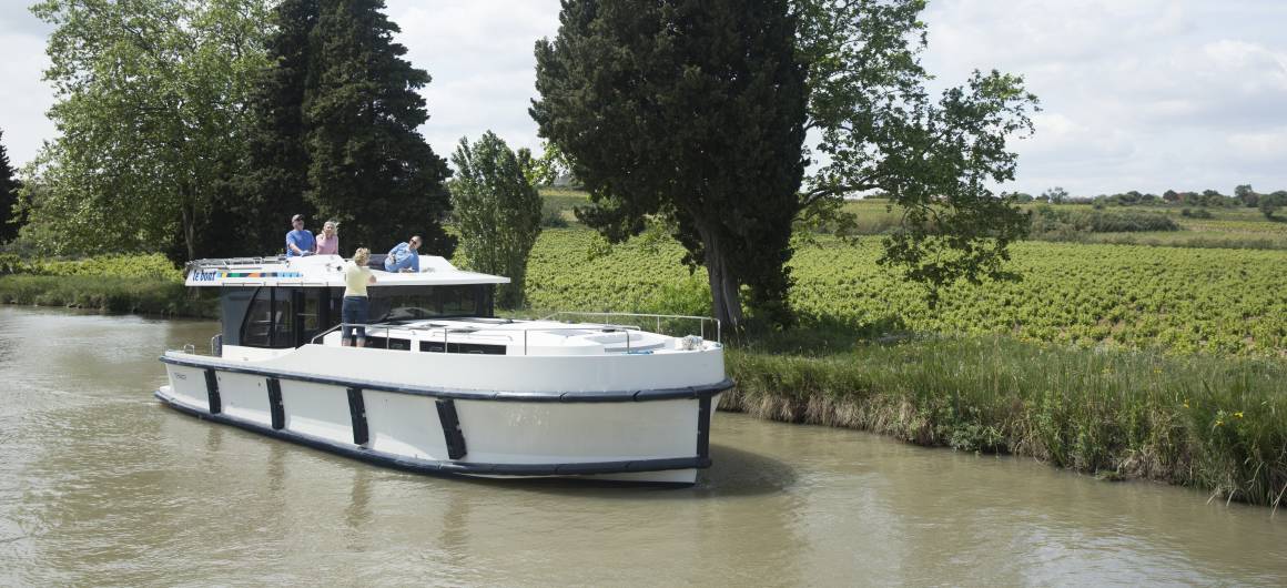 A canal boat glides past golden fields and peaceful countryside on the Canal du Midi in southern France.