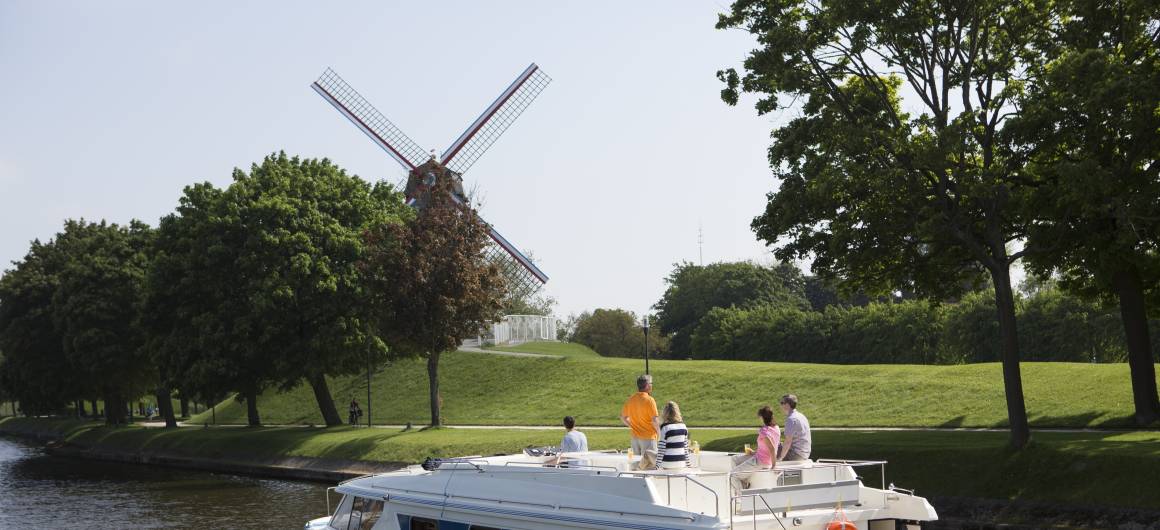 Family boating past a traditional windmill along the canal in Bruges, authentic Flemish experience in Belgium.