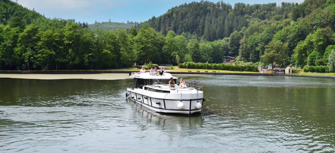 Bateau Horizon glissant sur un lac paisible entouré de forêt luxuriante et de collines lointaines en Alsace.