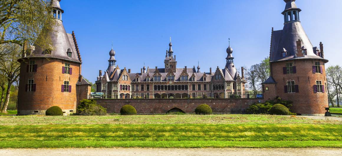 Gaasbeek Castle with its fairytale towers and manicured lawn under blue skies, historic attraction in Flanders, Belgium.