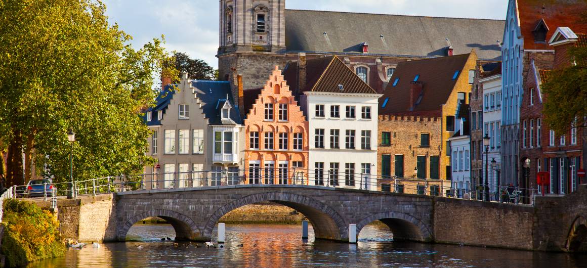 Stone bridge over Bruges’ canal with church and historic houses, timeless beauty of Belgium’s medieval town.