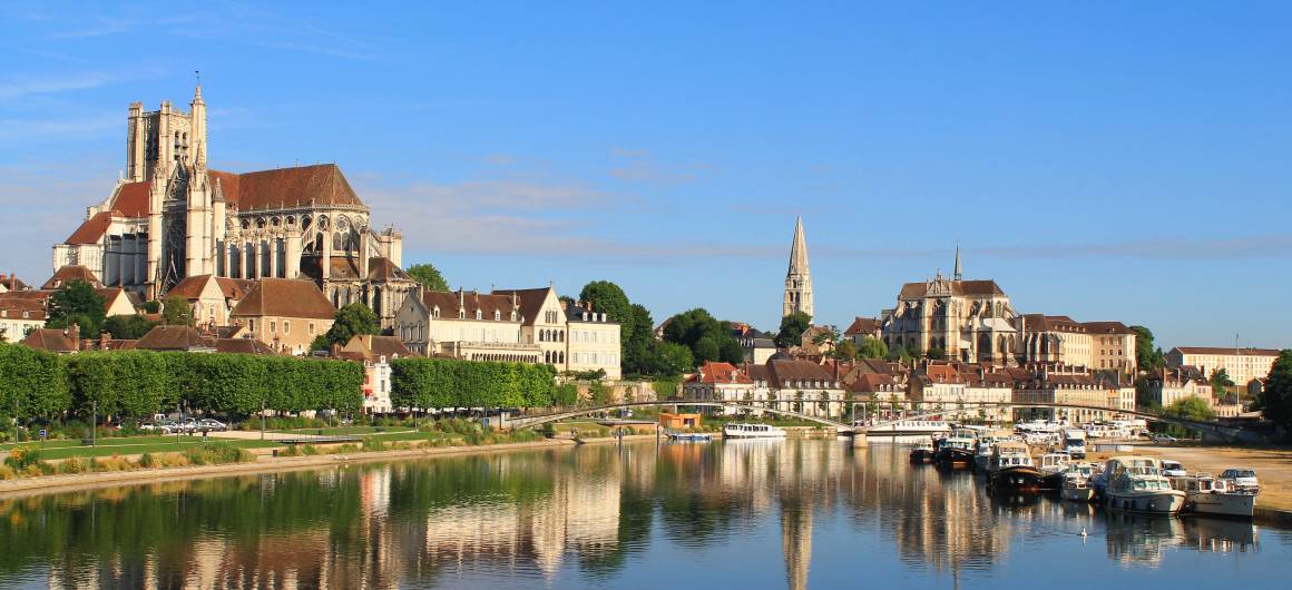 Riverside view of a historic Burgundian town with stone bridges, gothic cathedrals, and moored boats.