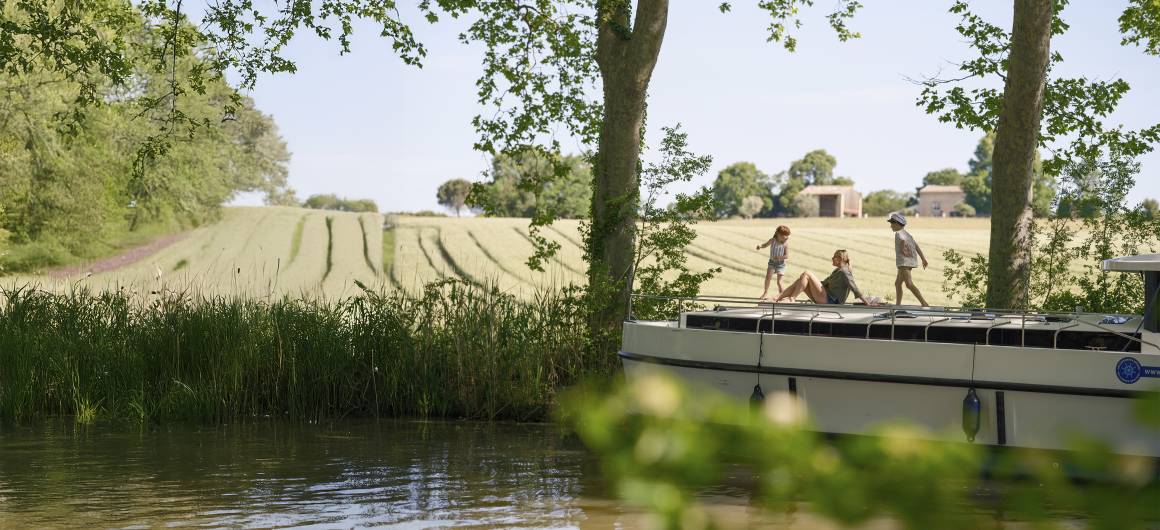 Two children play while their mum relaxes on the boat, enjoying a sunny day along the riverbank.