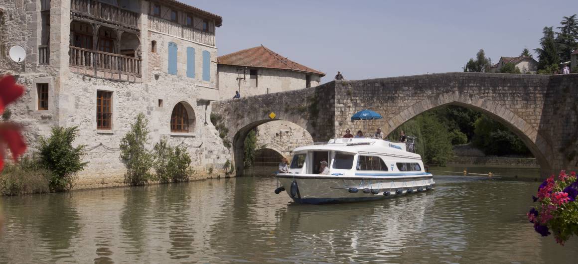 Un bateau glisse sous un pont de pierre médiéval en Aquitaine.