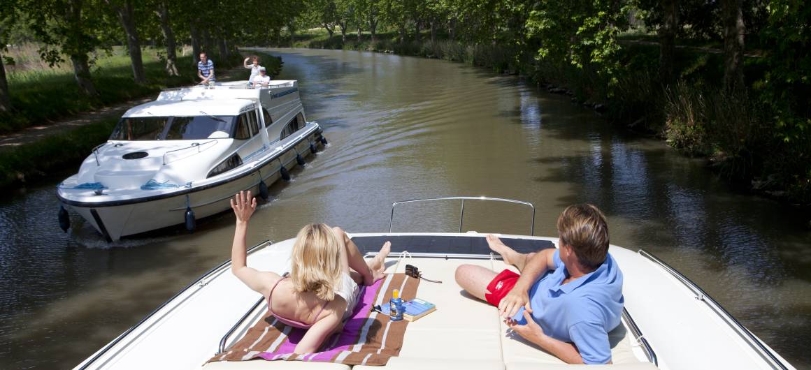 Boaters relax and sunbathe on the deck of a canal boat during a warm summer day on the Canal du Midi in France.