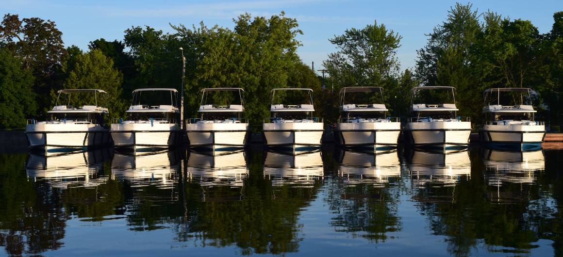 A row of Horizon boats lined up at the Le Boat base on the Rideau Canal, their reflections mirrored in the calm water.
