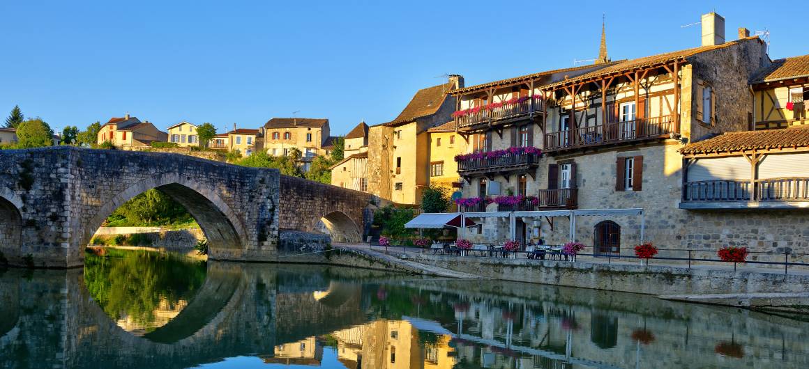 Terrasses de café surplombant la rivière près d’un pont historique en Aquitaine.