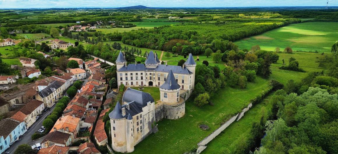 Majestueuze luchtfoto van het Château de La Rochefoucauld, omringd door weelderig platteland en een schilderachtig dorp.