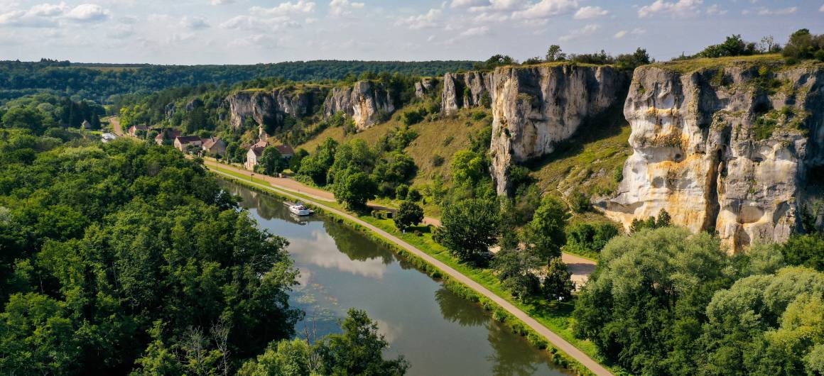 A boat travels along a river beneath dramatic limestone cliffs in Merry-sur-Yonne, Burgundy.