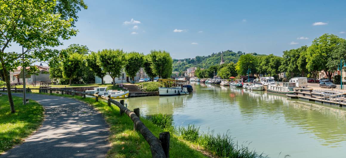 Ville ensoleillée en bord de rivière avec bateaux amarrés et promenades ombragées à Moissac.