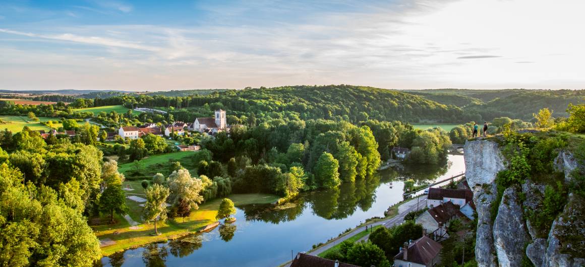 Hikers admire the view from a clifftop overlooking a winding river and forested valley in Burgundy.