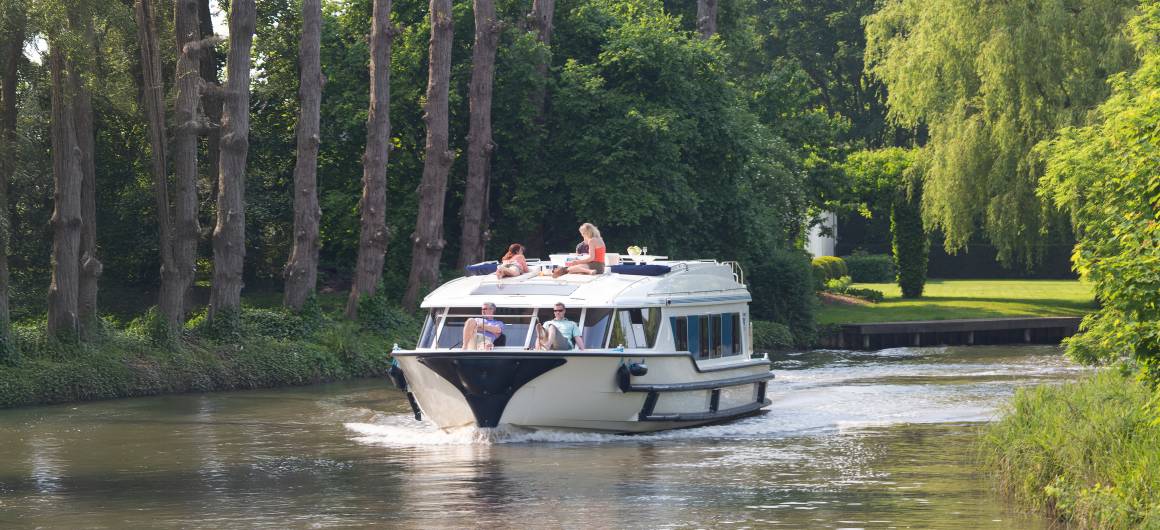 Group enjoying a boat ride on a tree-lined canal in Flanders, Belgium, ideal for relaxing holidays on the water.