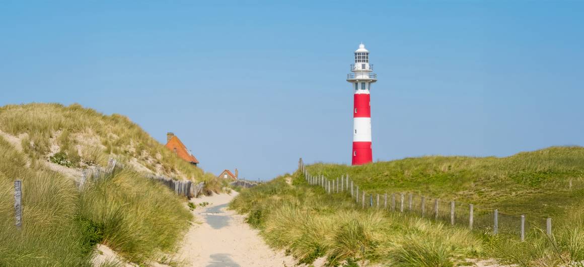 Scenic footpath through sand dunes leading to a lighthouse, Belgian coastal beauty in the Flanders region.