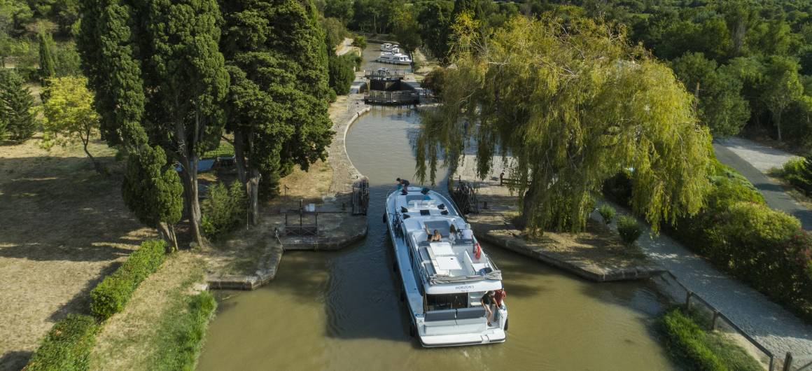 A canal boat approaches a traditional lock on the Canal du Midi along the Canal du Midi, offering a classic French boating experience.