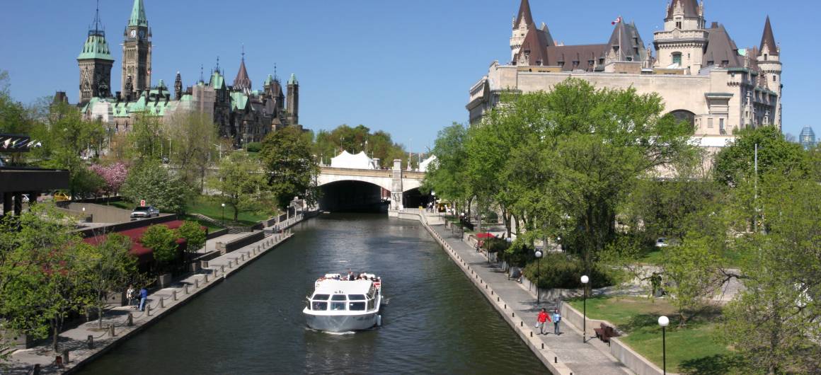 A sightseeing boat glides along the Rideau Canal in Ottawa, with the Canadian Parliament buildings rising in the background.