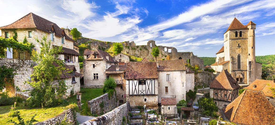 Traditional stone houses and a Romanesque church in a hilltop village along the Lot River under a vibrant sky.
