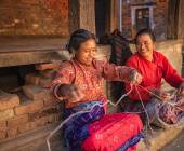 Nepali women spinning a wool in front of the house.