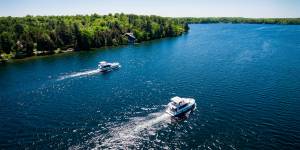 Due barche Horizon navigano su acque azzurre scintillanti lungo un tratto alberato del Canale Rideau in Ontario, Canada.