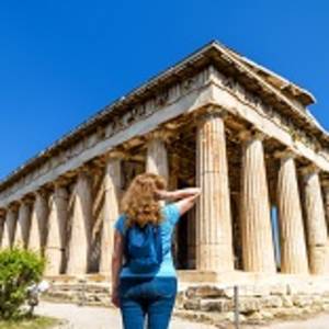 Young woman looks at Temple of Hephaestus, Athens, Greece. This ancient Greek structure is one of main landmarks of Athens.