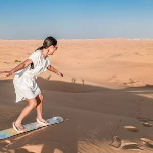 Frau auf einem Sandboard in einer Dünenlandschaft