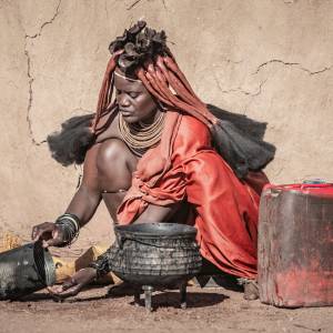 Auf dem Boden kniende Frau vom Stamm der Himba, die ihr Essen zubereitet