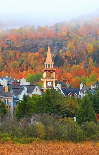 Blick auf die Kirchturmspitze des Dorfes Mont Tremblant vor der Kulisse eines nebelverhangenen Herbstwaldes